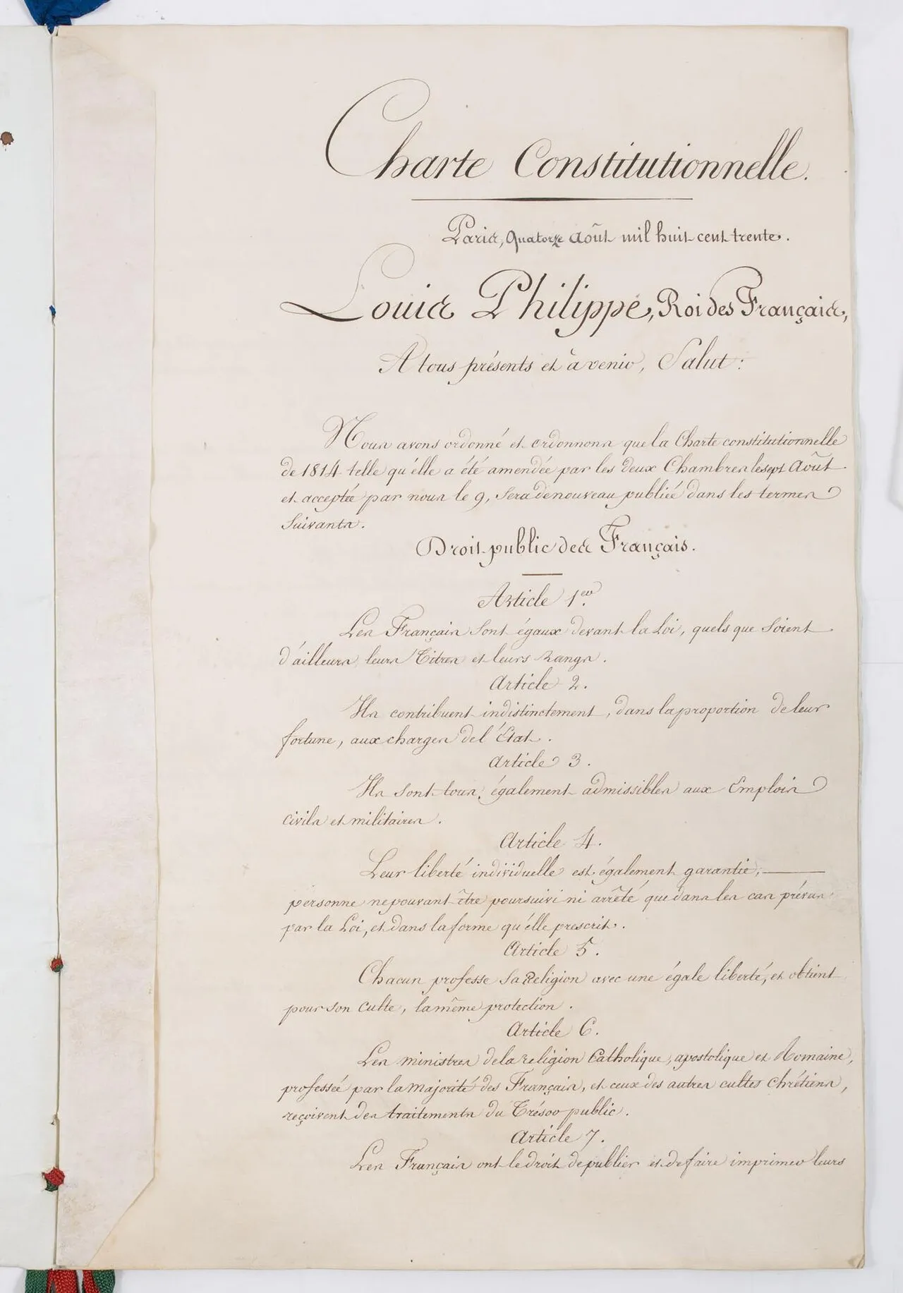 Page manuscrite à l'écriture calligraphiée, intitulée « Charte constitutionnelle », datée de Paris, quatorze août 1830, au nom de « Louis-Philippe, Roi des Français », suivie des premiers articles ; des rubans de soie dépassent sur le bord gauche.