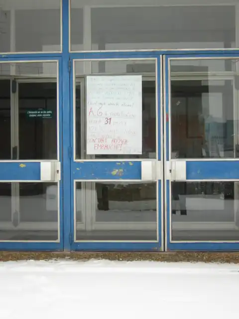 Affiche manuscrite scotchée sur la porte vitrée bleue d'un bâtiment universitaire, sol enneigé au premier plan.